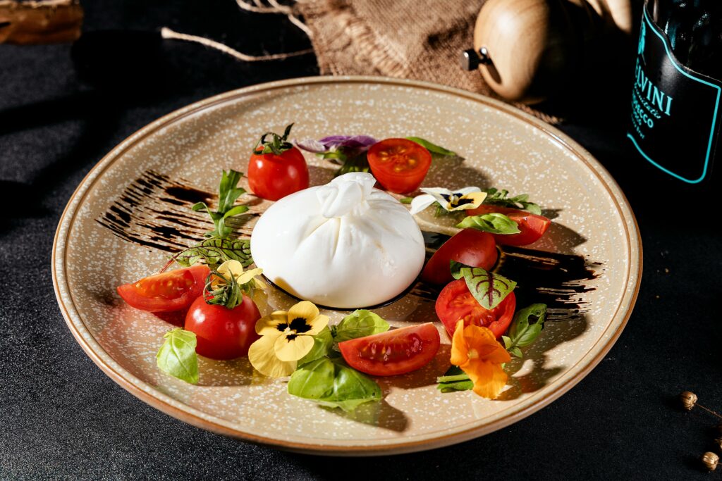 Elegant Caprese salad featuring fresh burrata, cherry tomatoes, basil, and edible flowers on a rustic plate.